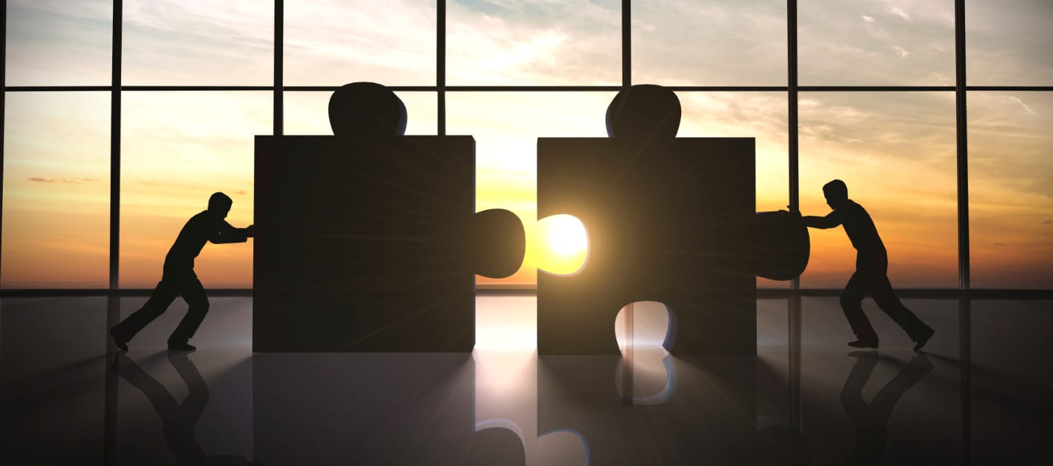 Silhouettes of two people pushing large puzzle pieces together in front of a sunset-view window, resembling printed pop-up tents. The sun glows brilliantly between the pieces, casting a radiant effect.