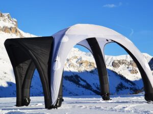 Inflatable black and white tent set up on a snowy mountain landscape with clear blue skies in the background.
