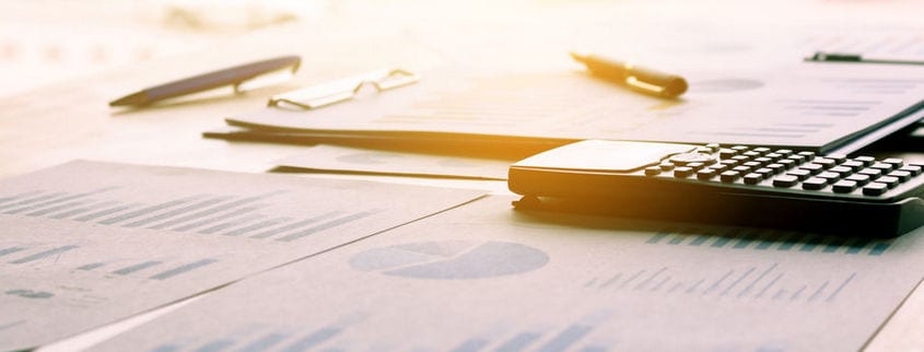 A desk cluttered with financial documents, graphs, a calculator, and pens. Sunlight filters in, creating a warm atmosphere.