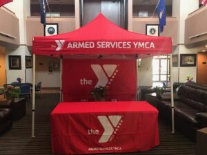 A red canopy and tablecloth with Armed Services YMCA and logo displayed in a room with flags and seating.