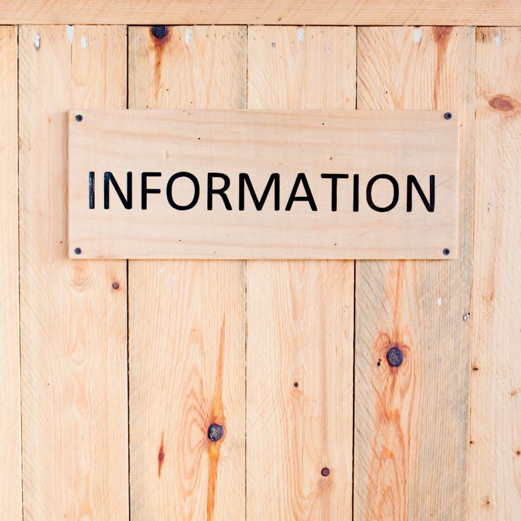 Wooden board with the word INFORMATION in black letters, mounted on a light-colored wooden wall. The wood has visible knots and grain patterns.