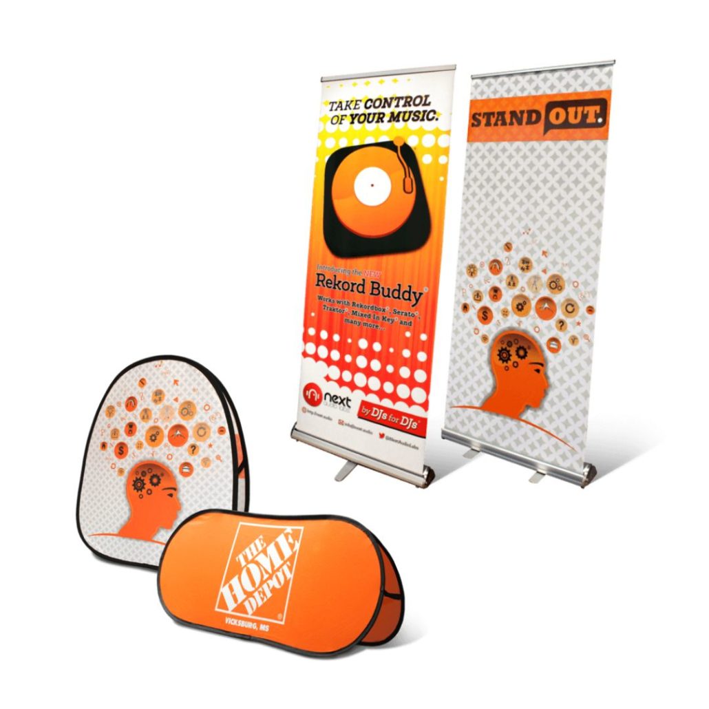 Display of promotional materials: two retractable banners and two pop-up signs with orange and white designs featuring stylized human head silhouettes and record graphics. Text includes Take Control of Your Music and Stand Out.