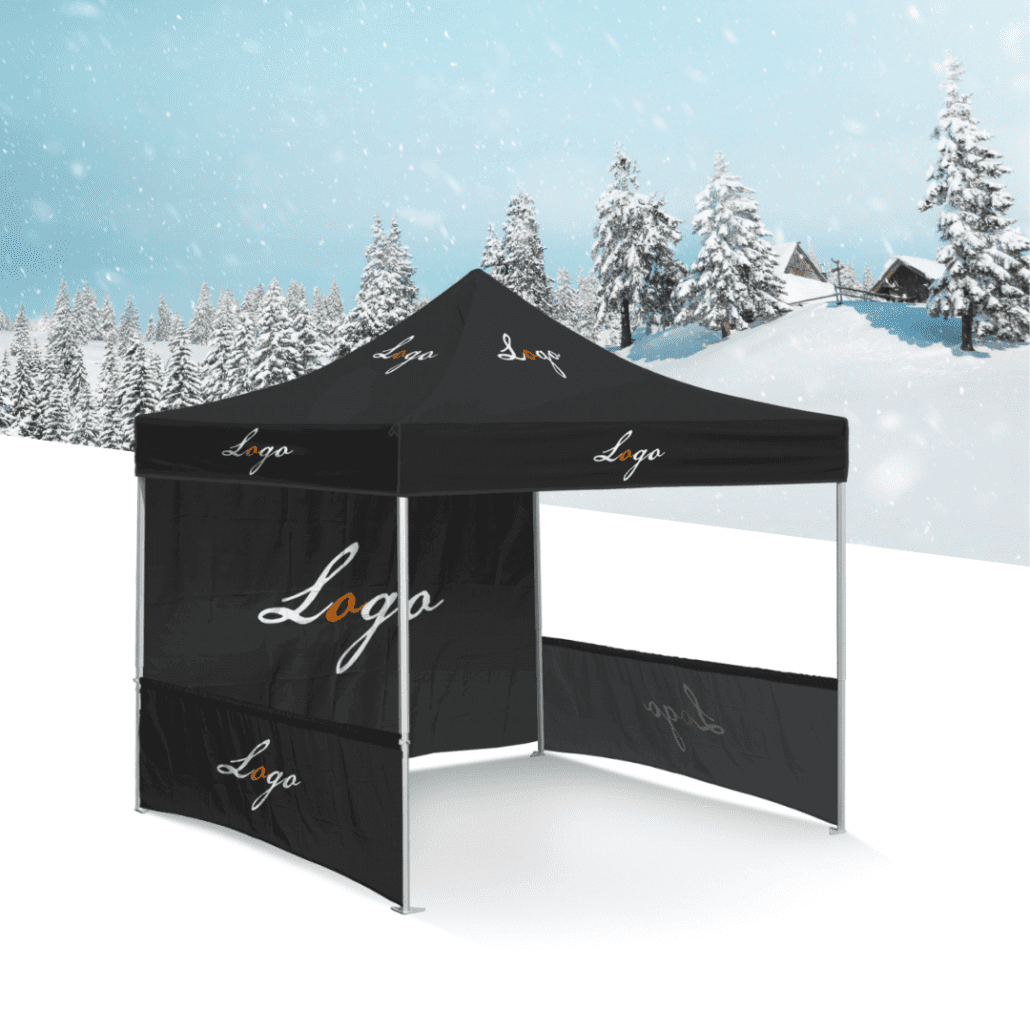A black soccer pop-up tent with branding on the canopy stands in a snowy landscape, surrounded by snow-covered trees and quaint wooden cabins. The clear sky above lets snowflakes gently fall, adding a touch of magic to this serene winter scene.