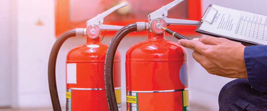 A person conducts a thorough maintenance check on two red fire extinguishers, holding a clipboard with a checklist. Ensuring the equipment is compliant with fire certificates for custom tents, the scene underscores a commitment to safety and preparedness.