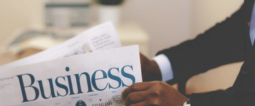 A person in a suit reads a business newspaper, its headlines partially visible, showcasing insights on the booming inflatables rental business. The focus remains sharp on the newspaper's Business section.