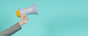 A person wearing a gray sleeve holds a white and yellow megaphone, reminiscent of inflatable marketing designs, against a turquoise background.