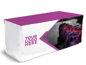 A fitted table cover featuring a fully printed design. The tablecloth has a purple top, white sides with "YOUR LOGO HERE" in purple text, and a geometric design showcasing a vibrant coastal town illustration.