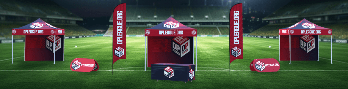 Outdoor sports field with red and white promotional tents and banners displaying the OPLeague.org logo. The setup includes tables and flags under stadium lights in an empty arena.