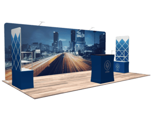 The 10'x20' Quick-N-Fit Booth - Package # 1219 showcases a cityscape backdrop featuring a highway at night. It includes blue and white displays with geometric designs and a prominent logo. The booth is set on a wooden floor and features a counter along with a stand for promotional materials.