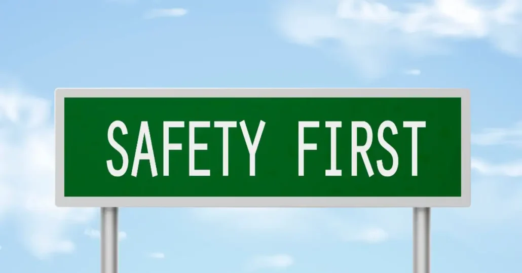 A green road sign with the words SAFETY FIRST in white capital letters stands against a blue sky with scattered clouds.