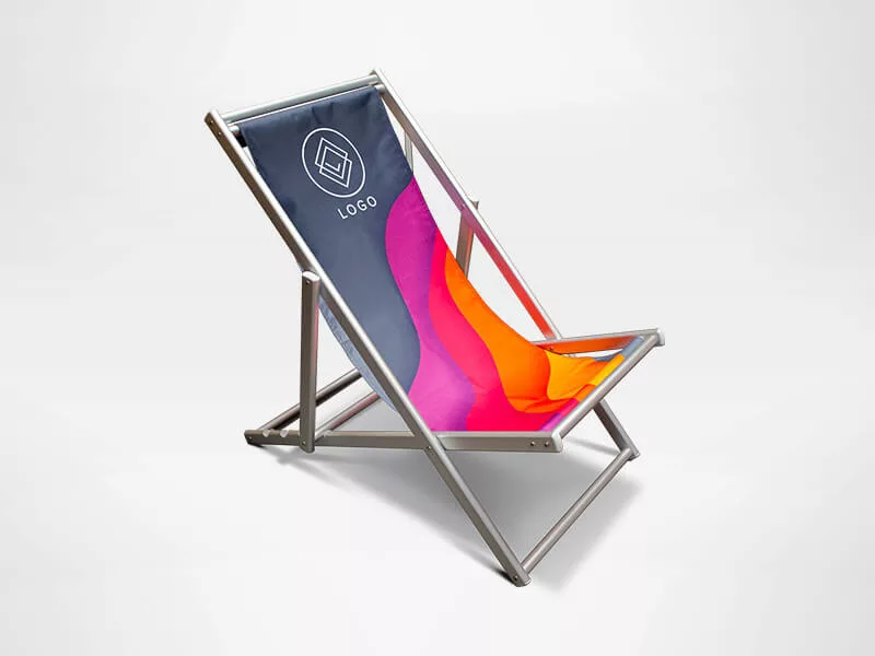 A colorful deck chair with a metal frame and a fabric seat. The seat has a vibrant design in shades of orange, pink, and blue, featuring a geometric logo on the backrest. The chair is set against a plain white background.