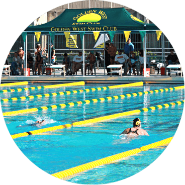 Swimming competition at an outdoor pool with several swimmers in lanes. A green tent in the background reads Golden West Swim Club. Spectators are seated behind the tent. Yellow lane dividers are visible.
