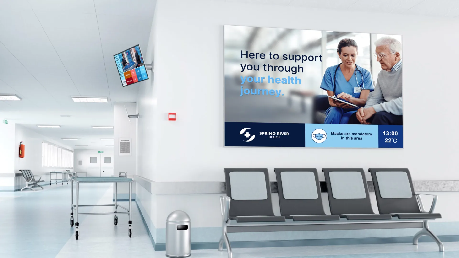 A hospital waiting area with empty chairs, a wall-mounted TV, and a trash can. A large poster on the wall shows a nurse assisting an elderly man, along with text about health support and a notice on mask requirements.
