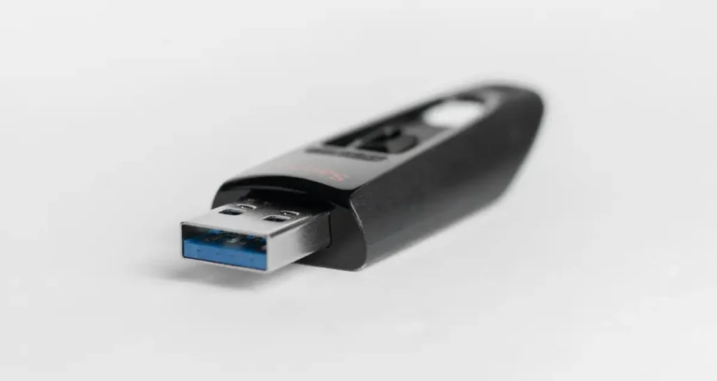 A close-up of a black USB flash drive with a blue connector tip, resting on a white surface.