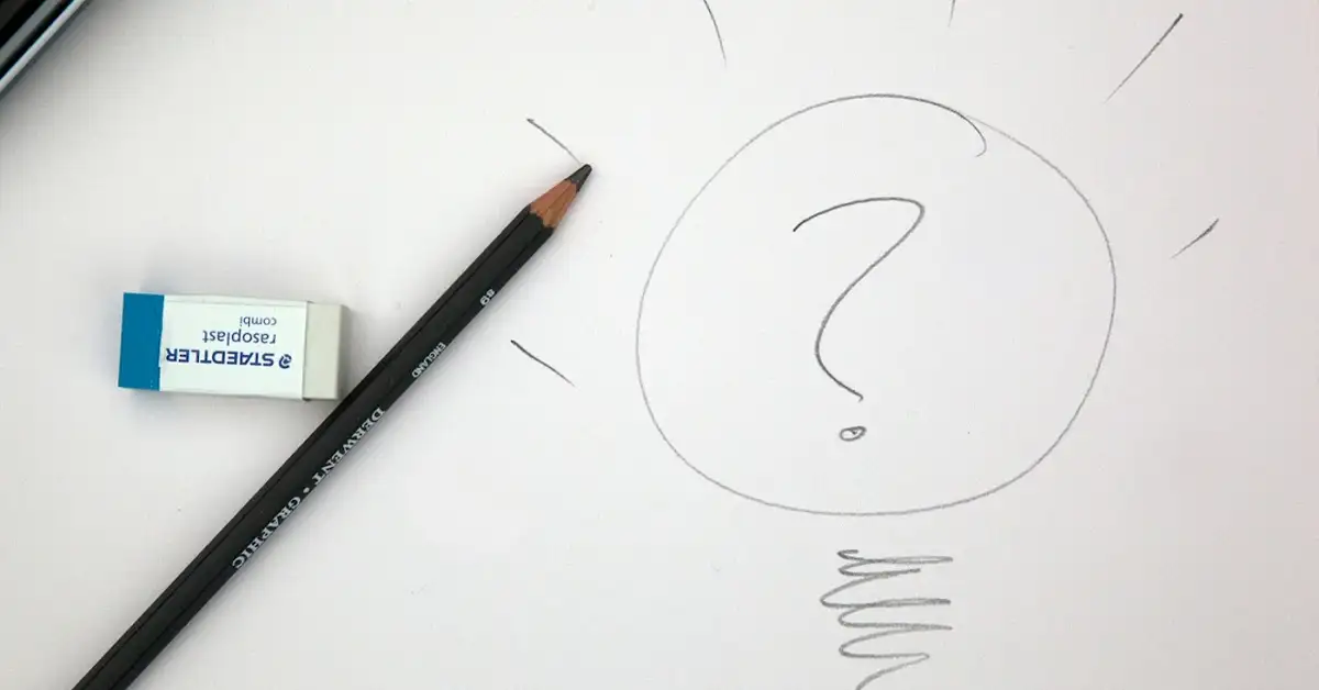 A pencil and an eraser are placed on a sheet of paper with a sketched light bulb containing a question mark inside. The light bulb is drawn with simple lines, symbolizing a concept or idea.