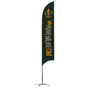A tall green flag with the Boy Scouts emblem at the top and the words #ADVENTUREON! in bold yellow and white letters, standing on a black pole with a cross-shaped base.