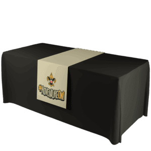 A black table covered with a beige runner featuring the Cub Scouts logo and the text #ADVENTUREON! in bold letters. The background is plain white.