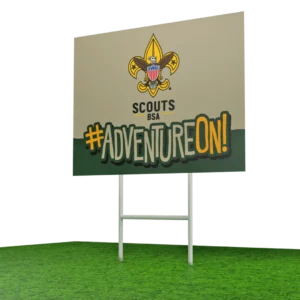 A sign on grass displays the Scouts BSA logo and the words #ADVENTUREON! in bold, colorful letters.