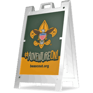 A sidewalk sign with the Boy Scouts of America logo, the words #ADVENTUREON! in bold, and the website beascout.org against a green and orange background.
