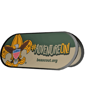 A promotional sign displays the Boy Scouts of America fleur-de-lis logo, the hashtag #AdventureOn! in yellow and white, and the website beascout.org on a green and tan background.