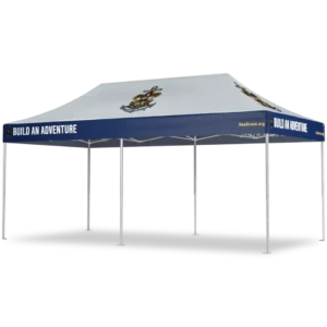 A large outdoor canopy tent with a blue trim displaying the words “BUILD AN ADVENTURE” and “SeaScout.org.” The roof features an anchor and sailor emblem, and the tent has six white legs.