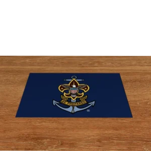 A blue mat with the Sea Scouts BSA emblem, featuring an anchor, an eagle with a shield, and a banner reading “Be Prepared,” is placed on a wooden surface against a black background.