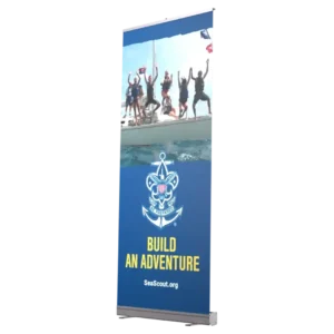 A vertical banner featuring a group of people celebrating on a sailboat, with the Sea Scouts logo and the text BUILD AN ADVENTURE and SeaScout.org on a blue background.