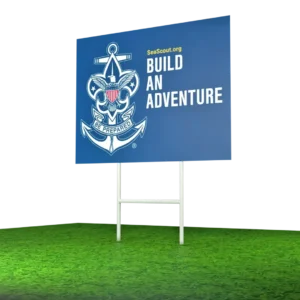 A blue billboard on green grass displays the Sea Scouts anchor emblem and the words SeaScout.org BUILD AN ADVENTURE and Be Prepared.