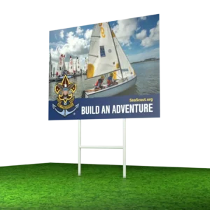 A Sea Scouts billboard shows teens sailing a small boat on the water under a partly cloudy sky. The sign reads “BUILD AN ADVENTURE” with the Sea Scouts logo and website SeaScout.org.