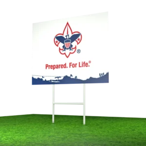 A sign with the Boy Scouts of America logo and the slogan Prepared. For Life. stands on grass, with a blurred background.