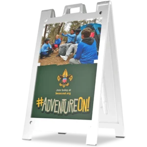 A sandwich board sign displays a photo of scouts sitting outdoors in a circle, above the Boy Scouts of America emblem, website link, and the text #ADVENTUREON! in bold yellow letters.