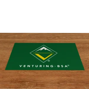 A green mat on a wooden floor features the Venturing BSA logo, which includes a stylized mountain inside a diamond, and the text VENTURING · BSA below it in white.