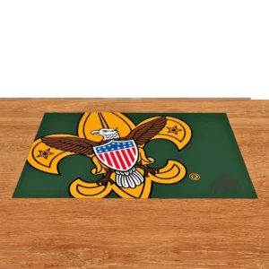 A green mat on a wooden surface featuring the Boy Scouts of America emblem: a gold fleur-de-lis with an eagle and shield in the center.
