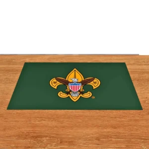 A green mat with the Boy Scouts of America emblem, featuring a gold fleur-de-lis, an eagle, and a red, white, and blue shield, placed on a wooden surface.
