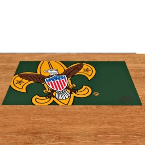 A green mat with the Boy Scouts of America emblem, featuring a gold fleur-de-lis, a bald eagle with a shield, and stars, placed on a wooden surface.