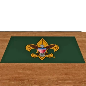 A green rectangular mat with the Boy Scouts of America emblem, featuring a gold fleur-de-lis and an eagle with a shield, placed on a wooden surface.