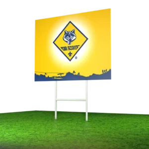 A yellow Cub Scouts sign with a blue wolf logo stands on a grassy area, supported by a white frame. The background is blurred with horizontal streaks of green, brown, and yellow tones.