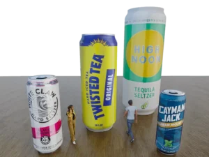 Two small human figures stand beside oversized Inflatable Slim Can, Constant Air replicas, making the cans look gigantic on a wooden surface against a plain black background.