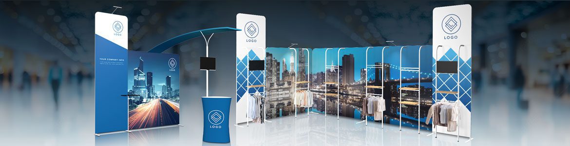 A modern trade show booth display with branded banners, digital screens, a counter, and clothing racks, set against a blurred exhibition hall background. The booth features blue and white geometric designs and cityscape images.