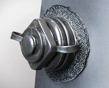 A close-up of a metal fastener with two handles attached to a textured circular patch on a fabric or rubber surface.