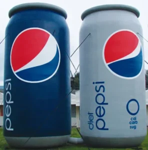 Two large outdoor structures shaped like Pepsi cans stand side by side; one is a regular blue Pepsi can, and the other is a gray Diet Pepsi can with 0 cal, carb, sug written on it.