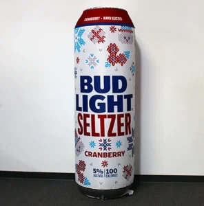 A tall can of Bud Light Seltzer Cranberry with festive snowflake designs, standing upright on a dark floor against a plain light-colored wall. The can displays 5% alcohol and 100 calories.