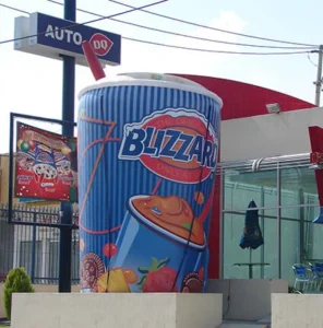A giant decorative Dairy Queen Blizzard cup stands outside a Dairy Queen restaurant, next to an Auto DQ drive-thru sign and outdoor seating area.