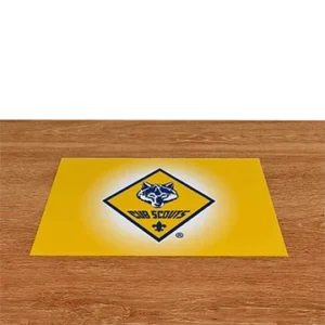 A yellow Cub Scouts sign with a blue wolf head logo and CUB SCOUTS text sits on a wooden surface against a black background.