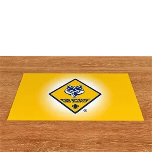 A yellow mat with the Cub Scouts logo, featuring a wolf head inside a diamond shape and the words Cub Scouts, is placed on a wooden floor.