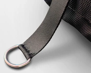 A close-up of a black fabric strap sewn onto a textured black bag, ending in a silver metal D-ring against a light background.