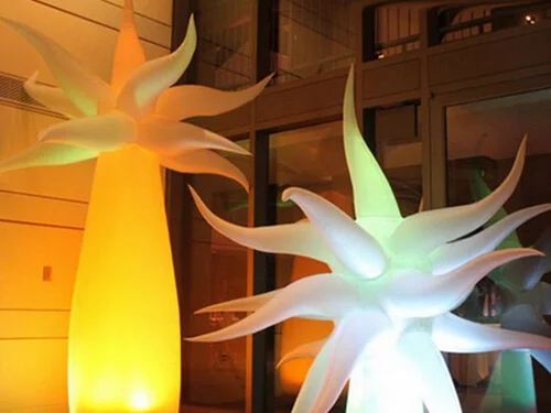 Two large, illuminated inflatable structures with spiky, starburst shapes, one glowing orange and the other green, are displayed indoors in front of glass doors and windows.