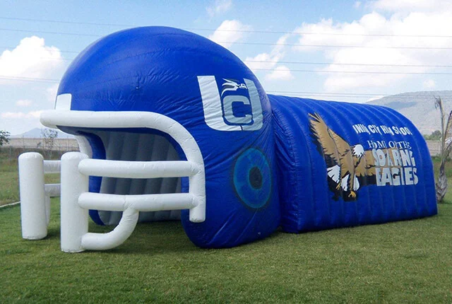 A large blue inflatable football helmet tunnel sits on grass, featuring a white facemask and eagle graphics with the text HOME OF THE GOLDEN EAGLES on the side.