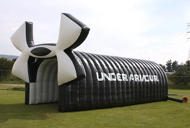 A large black and white inflatable tunnel with the Under Armour logo and brand name on the side is set up on a grassy field.