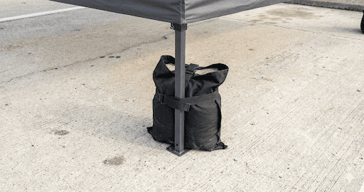 A black sandbag secures the leg of a canopy tent on a concrete surface, helping to stabilize the structure.